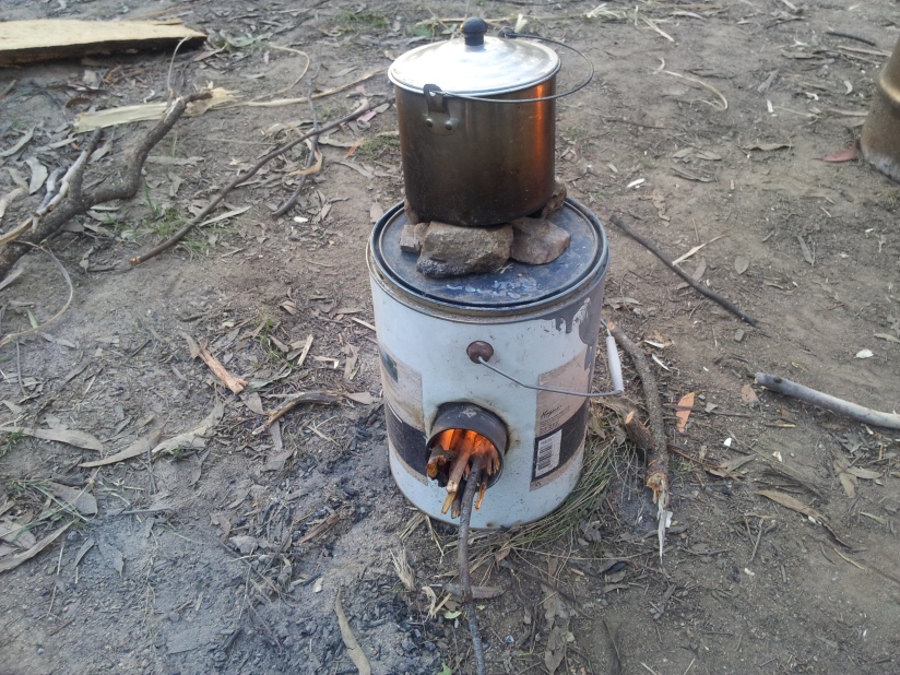 Rocket stove made from a paint can and 3 smaller 300 gram food cans. Small rocks used to create gap between pot and stove